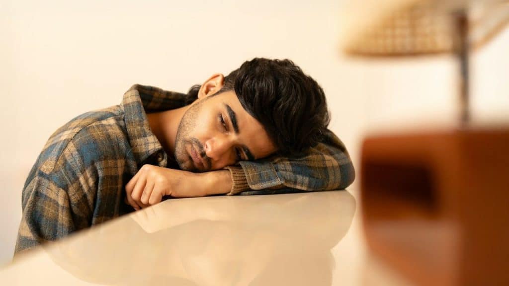 A man in a plaid shirt rests his head on his arm on a white surface.
