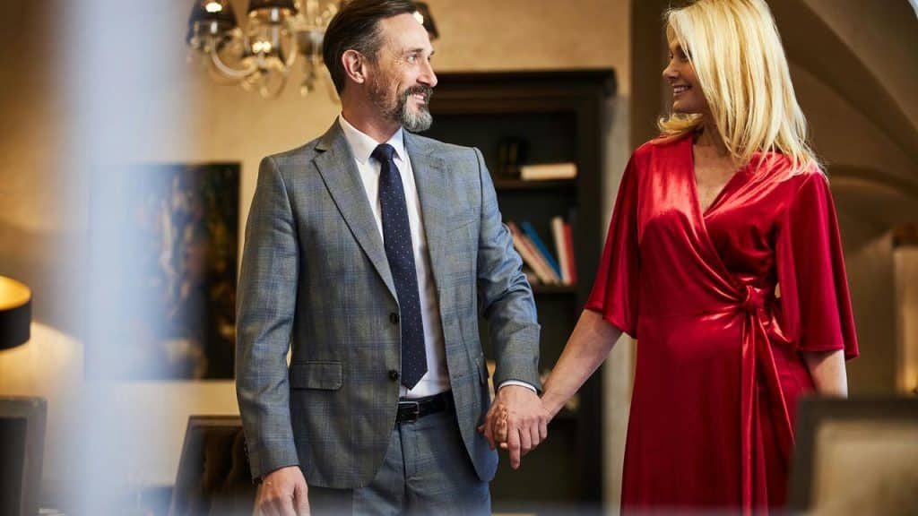 A couple dressed elegantly holding hands and smiling at each other.
