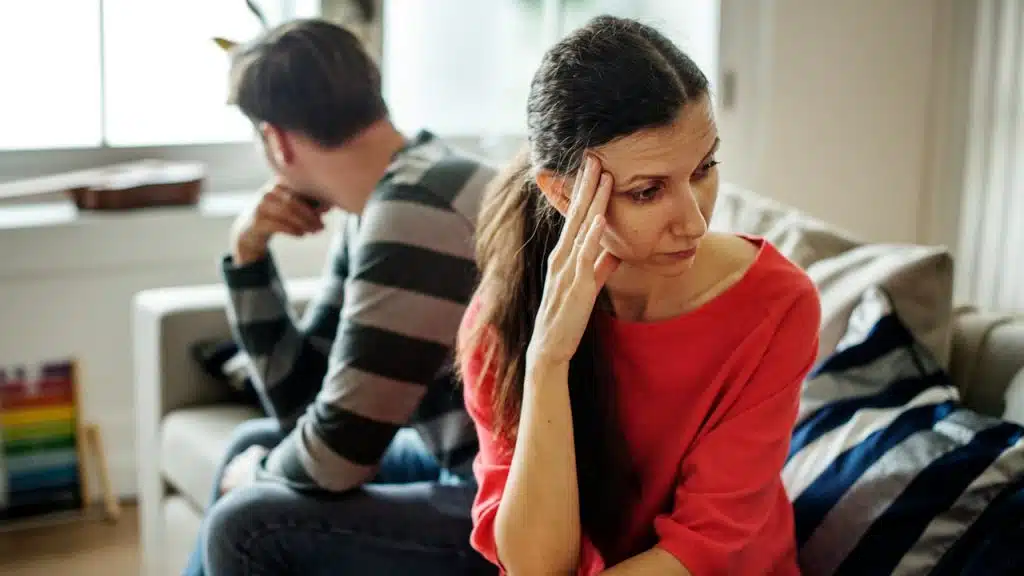 A couple looking away from each other while they sit on a couch.