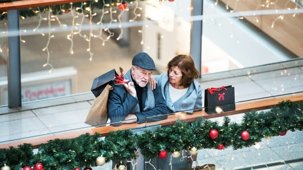 A senior couple talking inside the mall, carrying shopping bags.