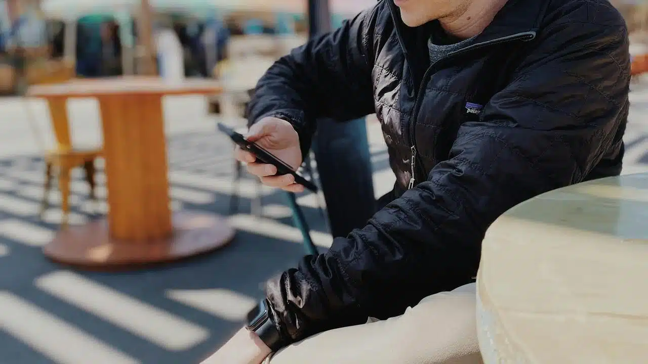 A person sitting at an outdoor café using a smartphone.