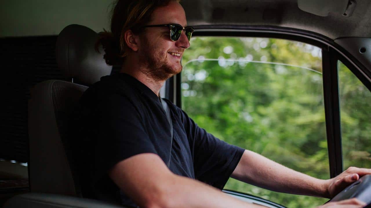 A man smiling while driving a vehicle through a green area.