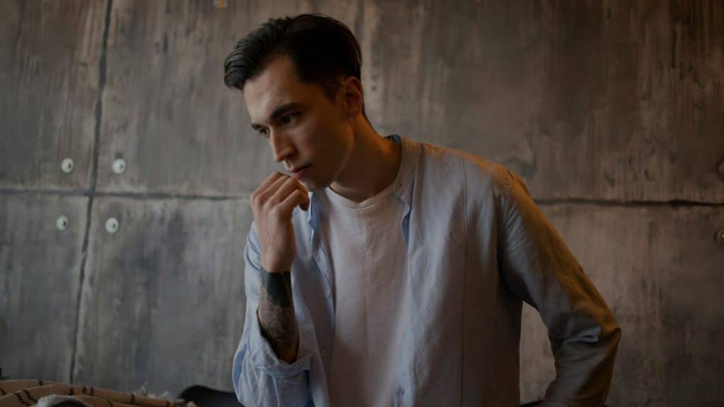 A young man in a light blue shirt looks down, resting his chin on his fist.