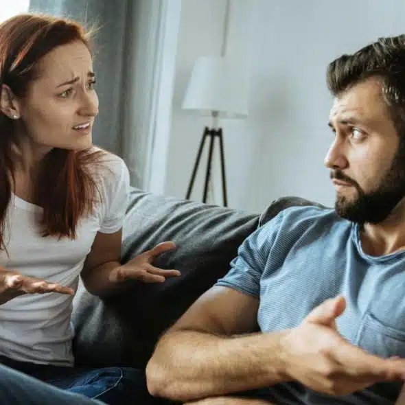 A distressed-looking woman and an annoyed man argue while sitting on a couch.