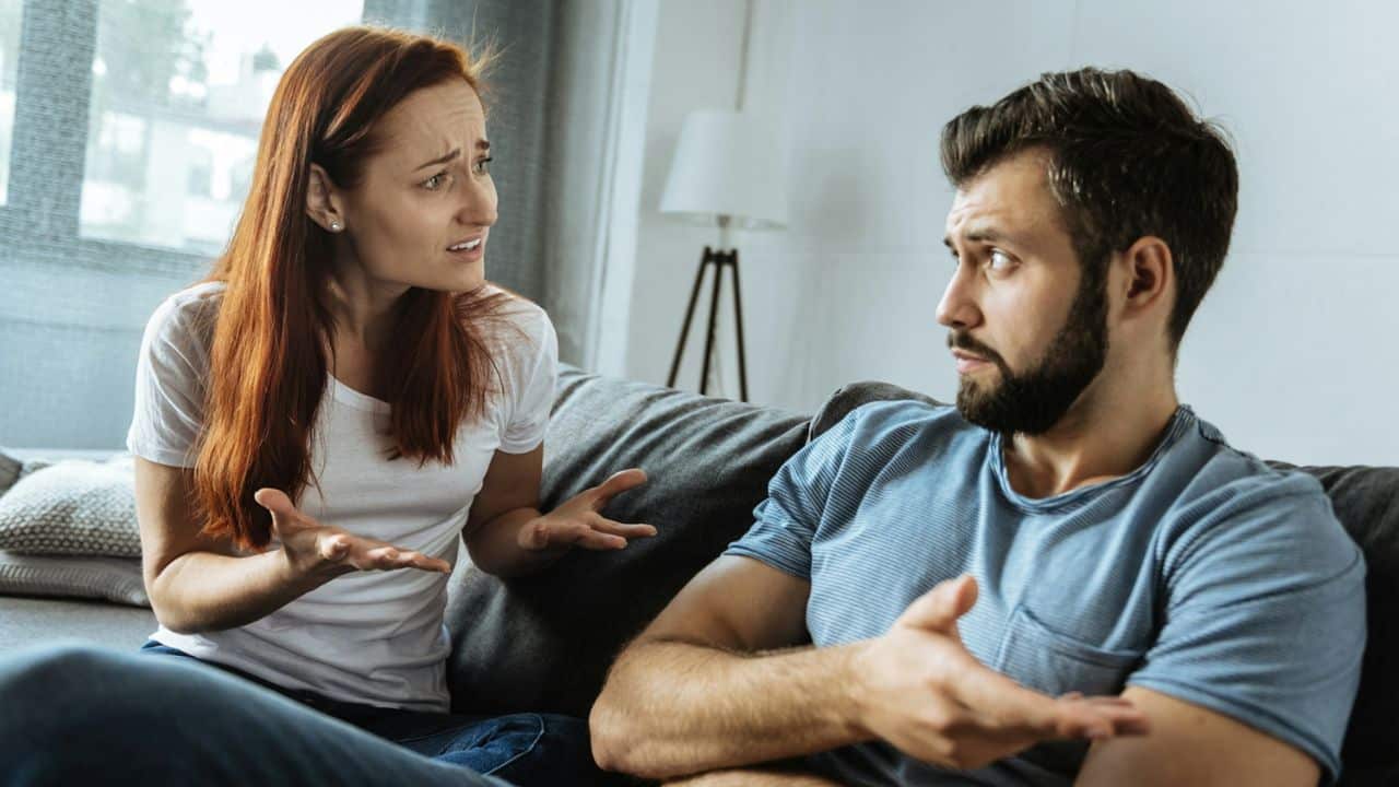 A distressed-looking woman and an annoyed man argue while sitting on a couch.