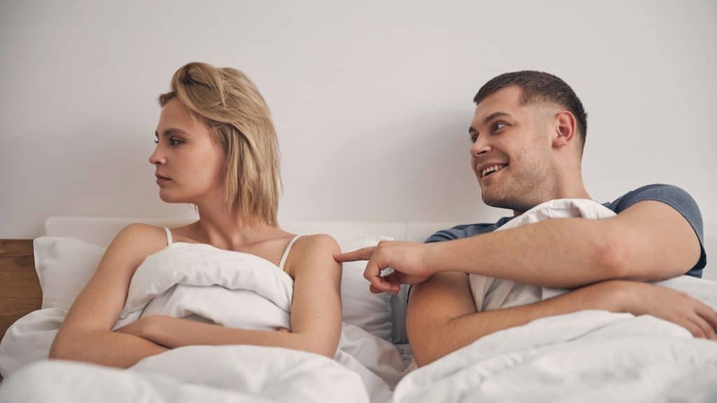 A man trying to please his angry wife while sitting on bed.