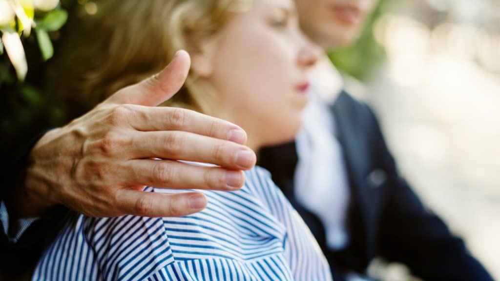 Close-up of a man's hand placed on a woman's shoulder or back in a comforting gesture.