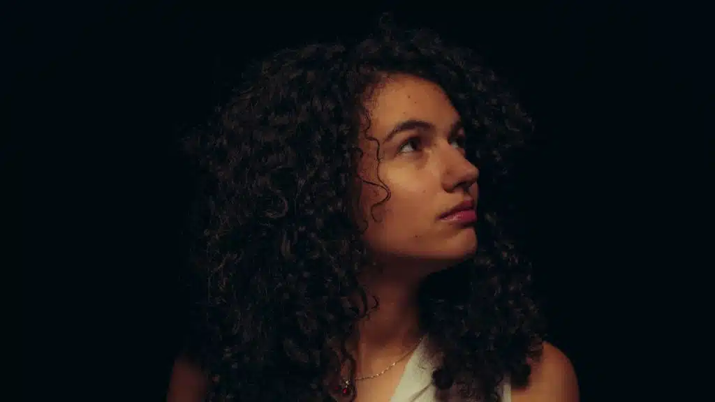 A woman with curly hair looking upwards with a somber expression.