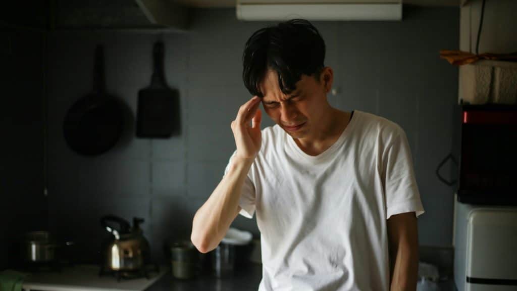 A man feeling a headache while he is standing in a kitchen.