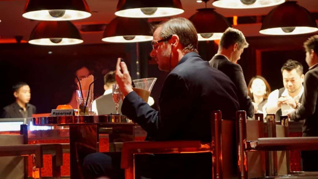 Man in a suit sitting at a reserved bar table, signaling a server.