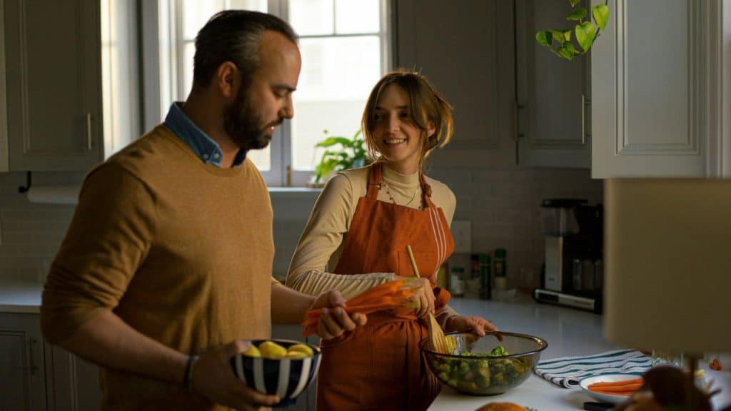 A man and woman are cooking together in a kitchen, both smiling and interacting happily.