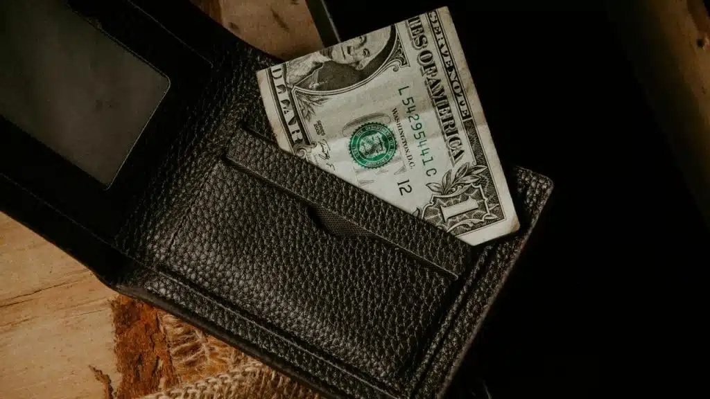 A dollar bill sticking out of a black leather wallet.