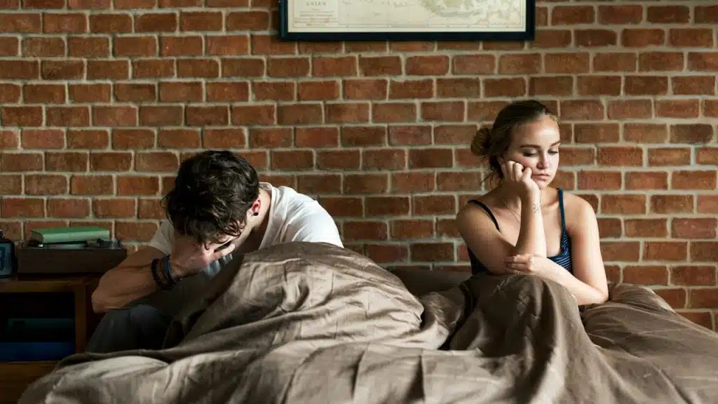 A man and a woman sitting next to each other in the bedroom.