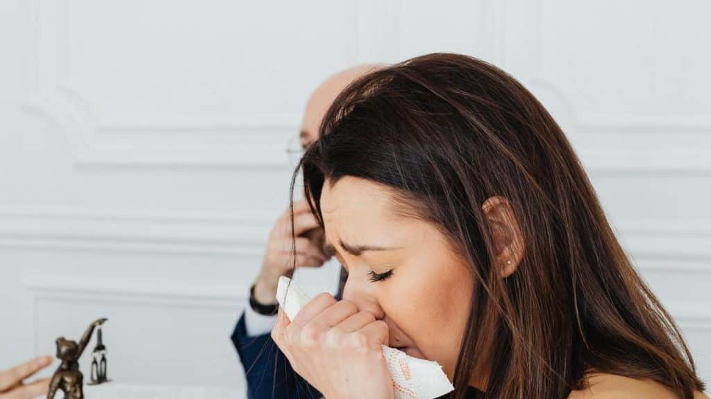 A woman crying into a tissue while a man sits in the background.