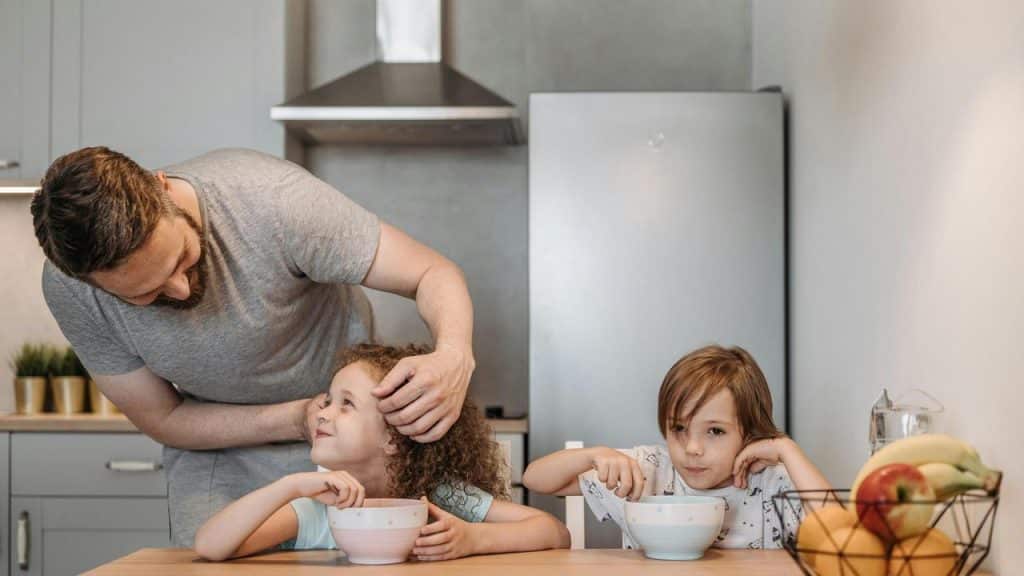 A father helping his kids during breakfast in the kitchen.