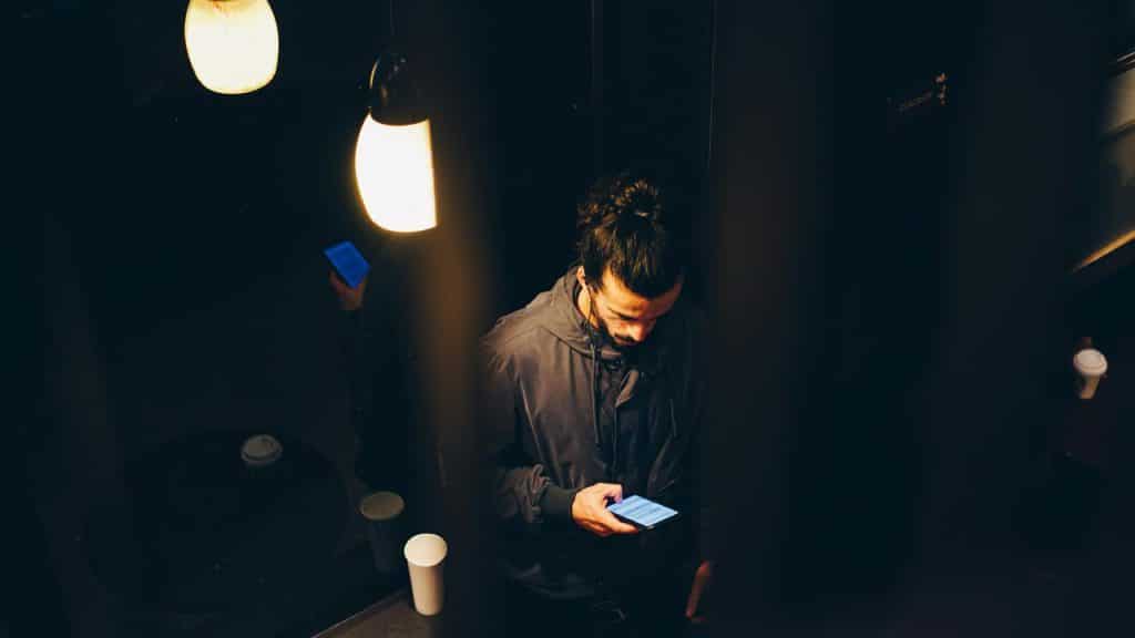A person standing indoors under warm lights while looking at a phone.