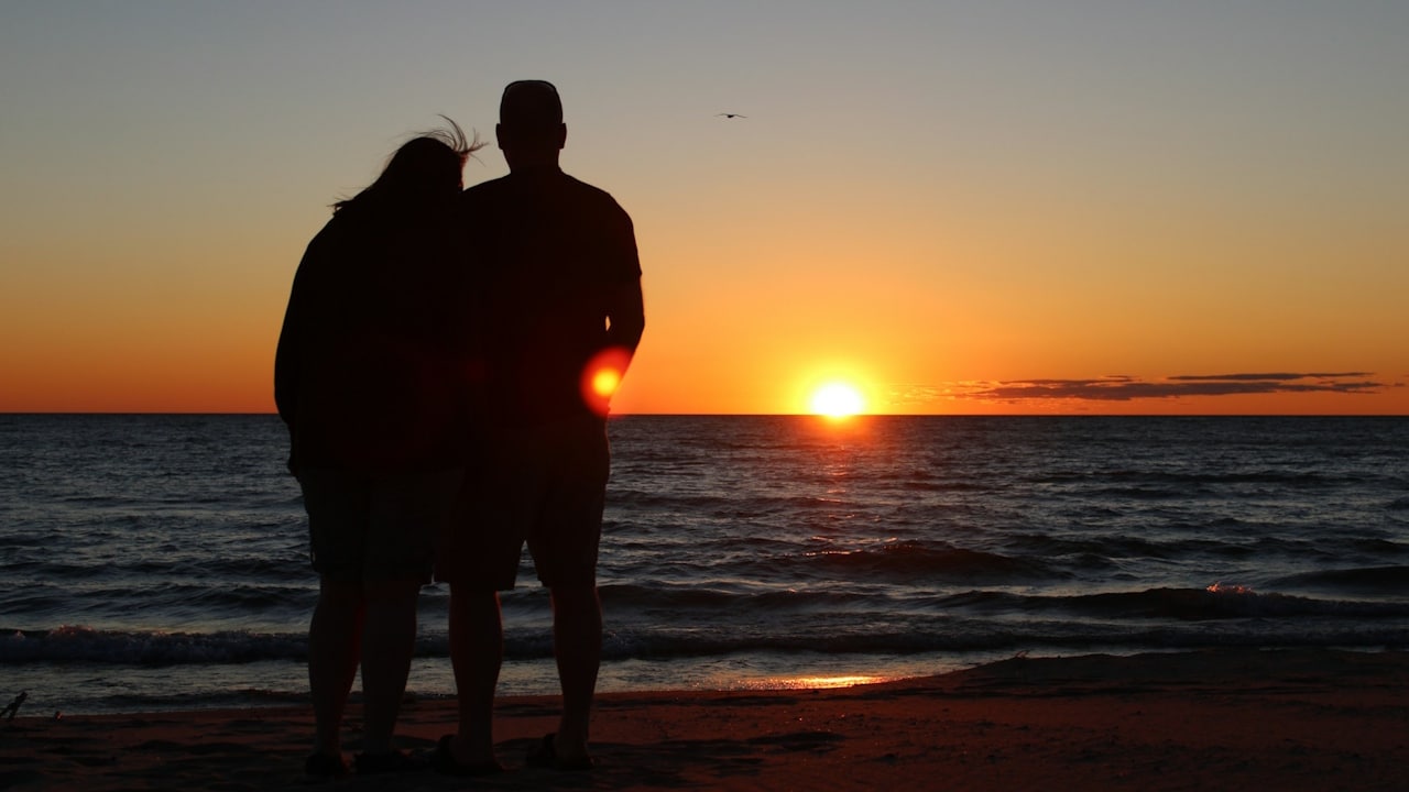 A silhouette of a couple standing on a beach, watching the sunset over the ocean.