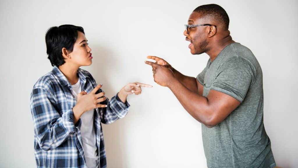 Man and woman standing, pointing fingers at each other in a heated discussion.