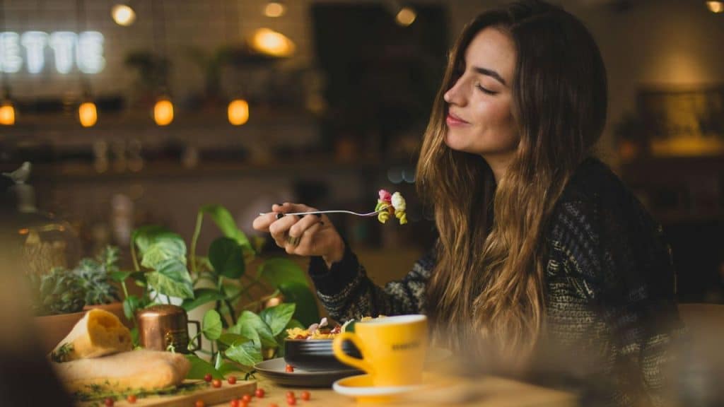 A young woman at a table savoring a forkful of food in a dimly lit restaurant.
