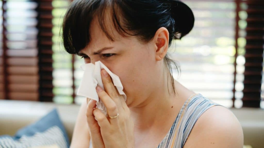 Close-up of a woman in a striped top blowing her nose with a tissue.