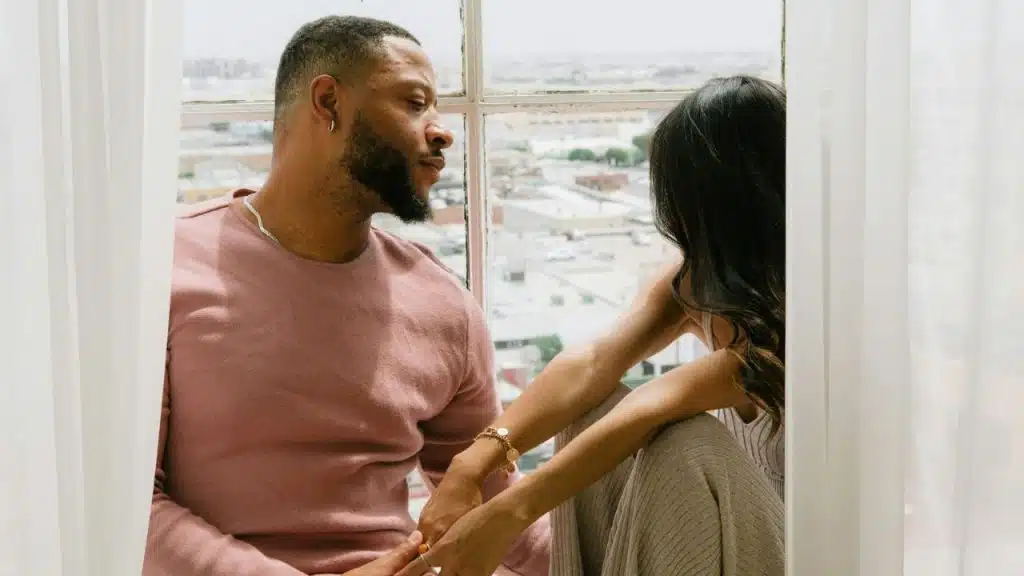 Man and woman holding hands while looking out a large window at a city.
