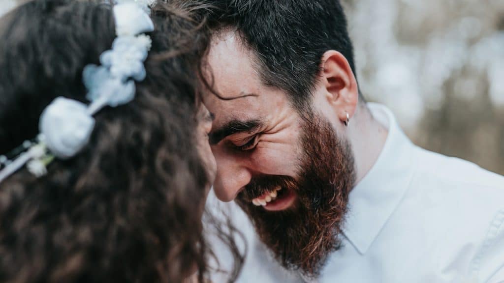 Close-up of a bearded man smiling brightly at a woman wearing a white shirt and an earring.