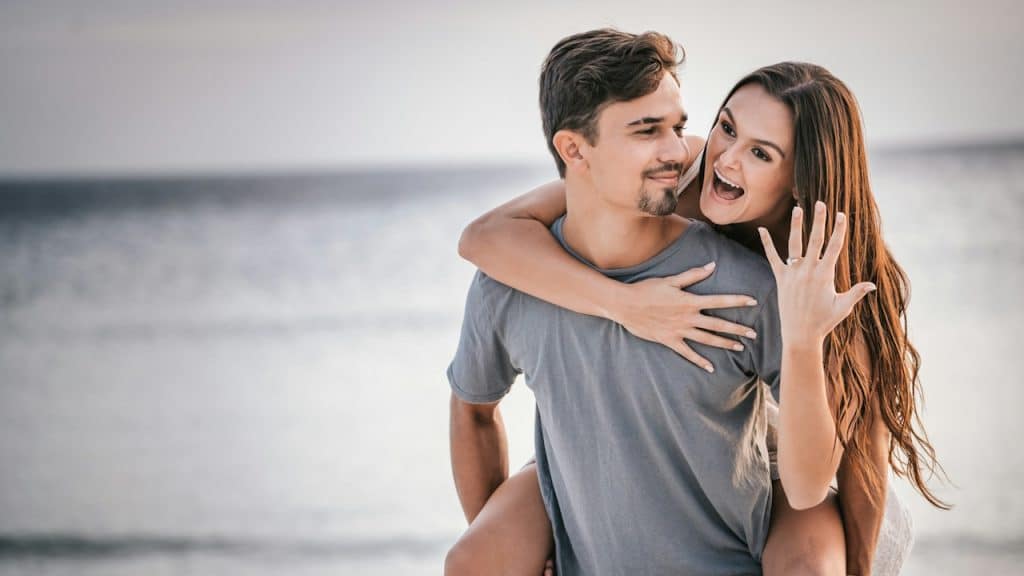 A man in a white crew-neck t-shirt hugging a woman in blue denim shorts.
