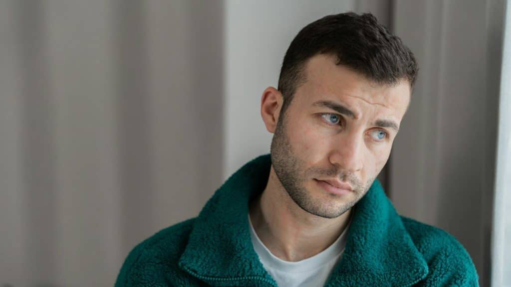A man in a green jacket with blue eyes is looking away from the camera.