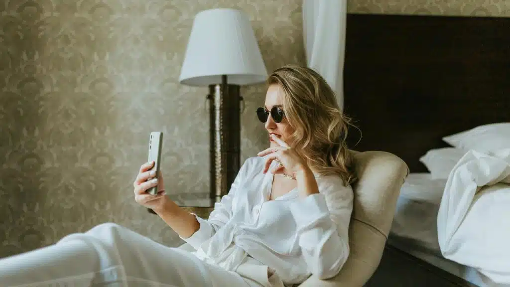 A woman wearing sunglasses sitting on a chair and looking at her phone.