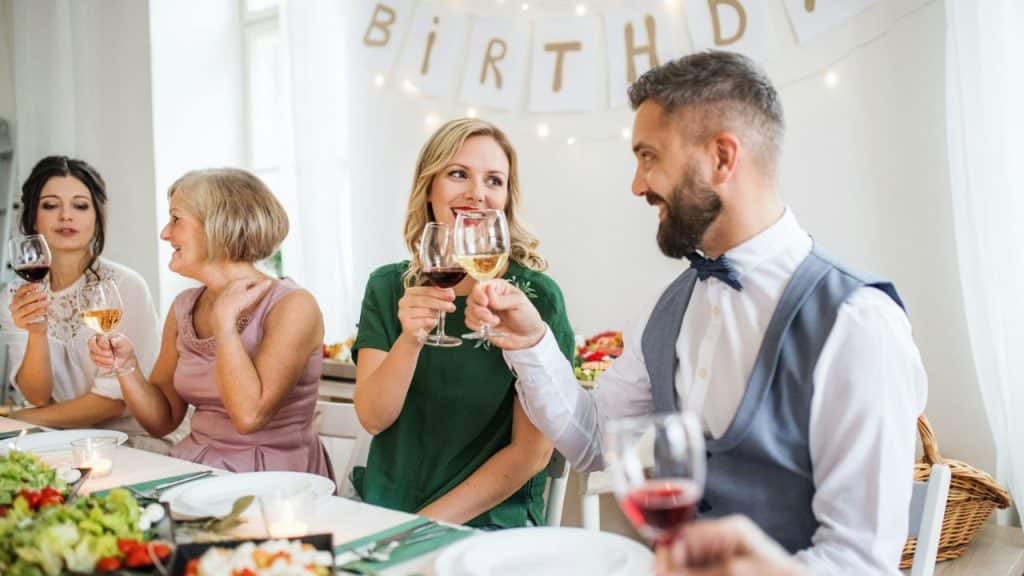 A group of adults toasting with wine at a decorated indoor birthday party table.