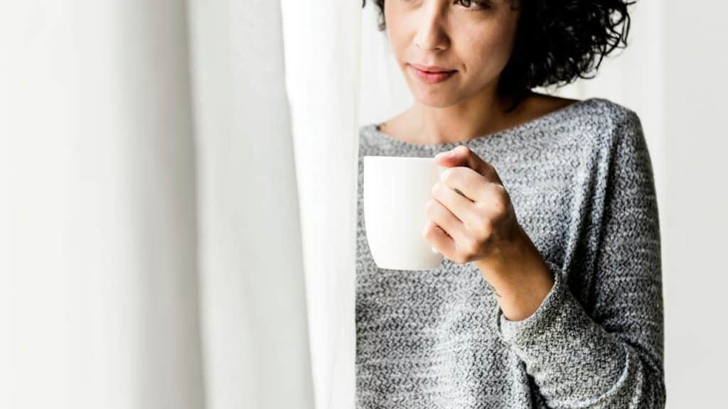 A person holding a mug by a window.