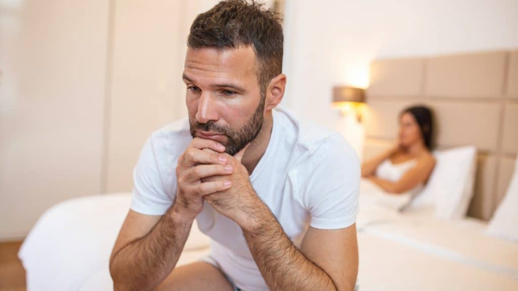 A young couple is having a problem—the guy is sitting on the bed and looking sadly away from his girlfriend.