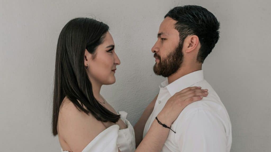 Man and woman in white shirts look at each other, woman's hand on man's shoulder.