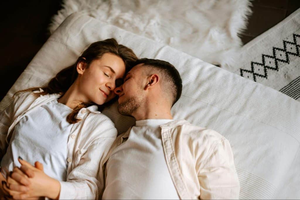A man and woman laying on the bed while holding hands 