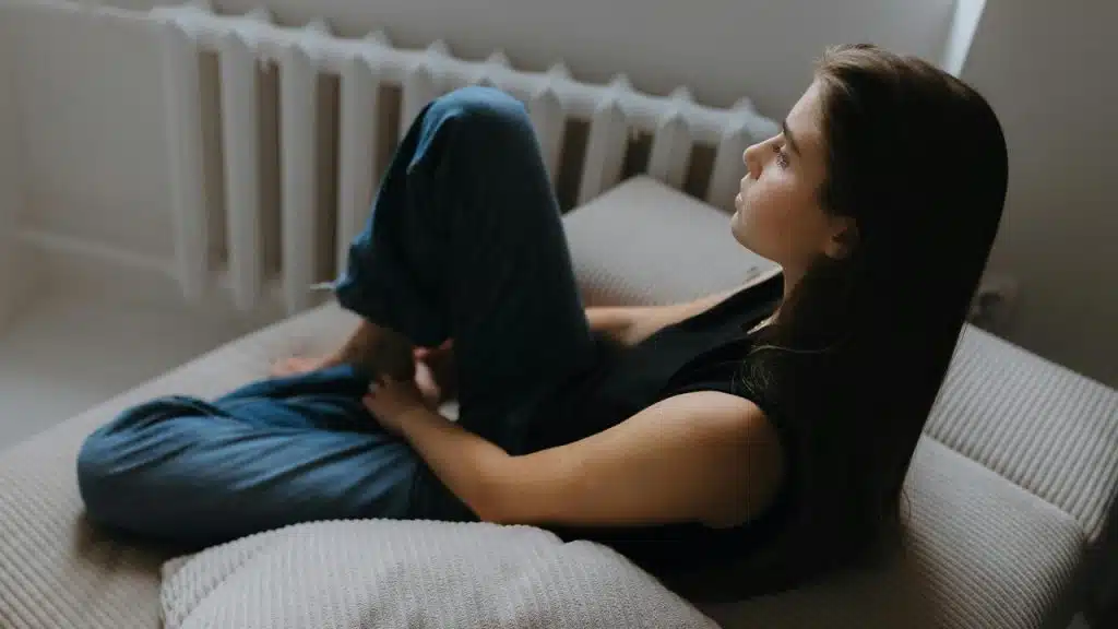 A woman sitting curled up on a couch, gazing thoughtfully to the side.