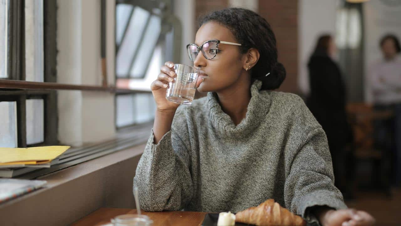A person wearing glasses sipping water at a café table.