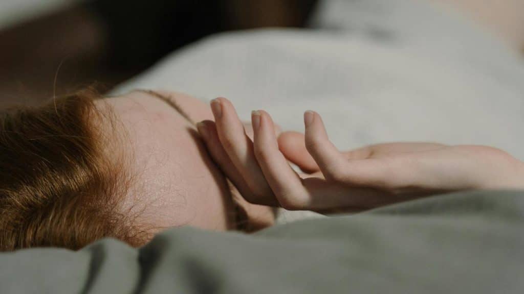 A close-up of a person lying in bed with a hand resting near their face.