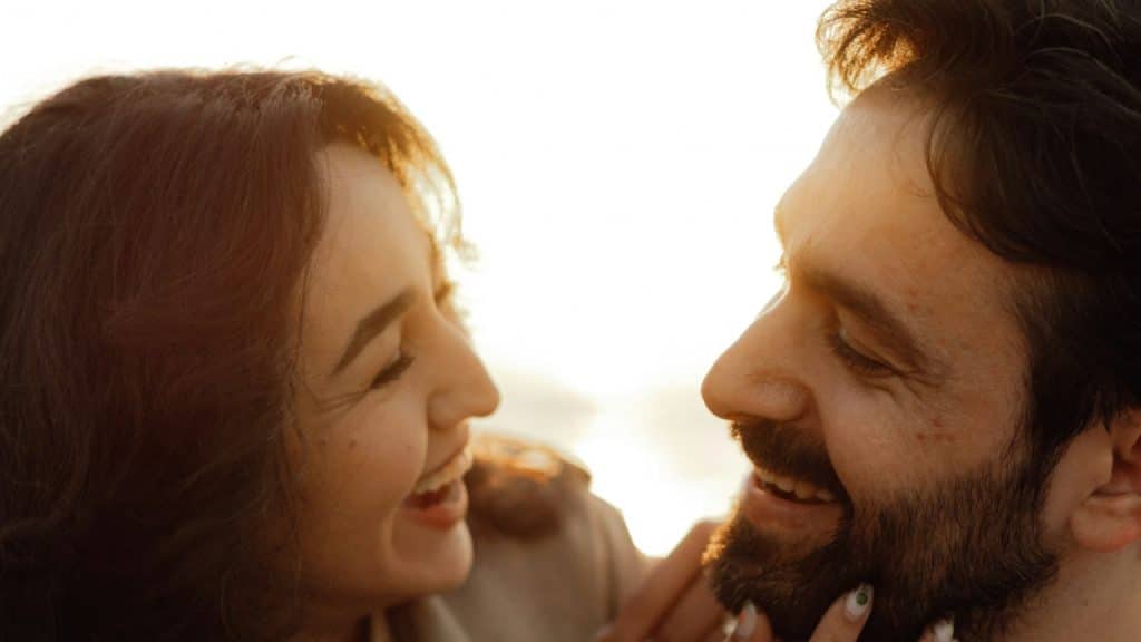 A couple laughing together while the woman strokes the man’s beard.