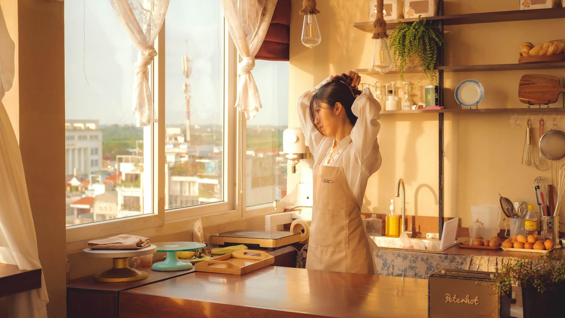 A woman in the kitchen and fixing her hair.