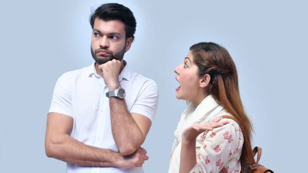 A woman shouting at a bearded man who looks to the side with a controlled expression.
