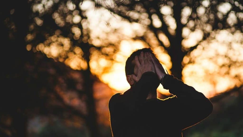 A silhouetted person covering their face at sunset among trees.