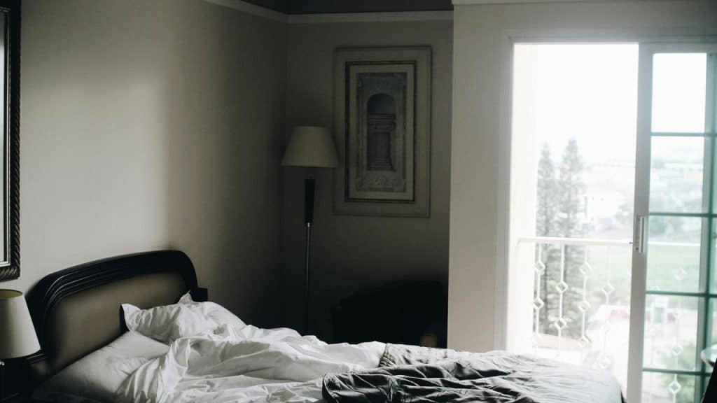 A messy bed beside a balcony door.