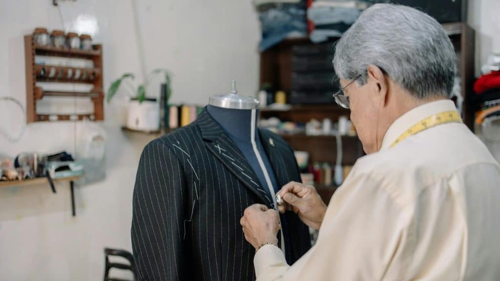 A tailor adjusting a pinstriped suit jacket on a mannequin in a workshop.