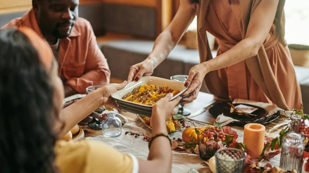 A person passing a dish of food at a dinner table.
