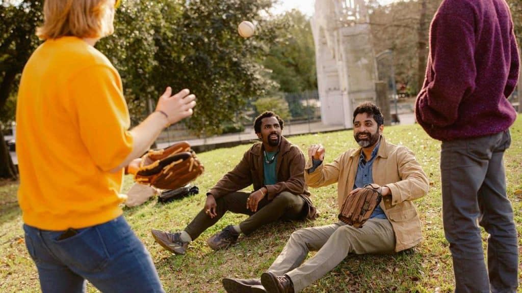 A group of friends playing catch with baseball gloves in a sunny park.