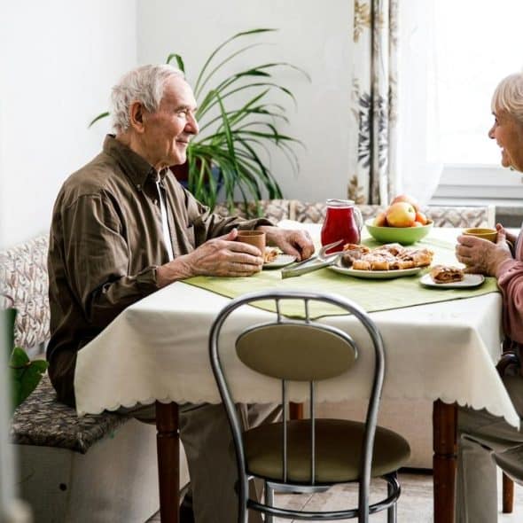 An elderly couple sitting at a kitchen table, smiling and sharing breakfast together.