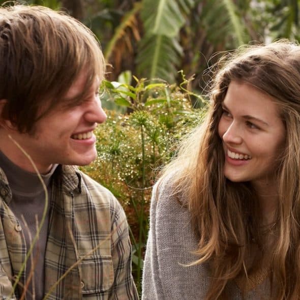A couple smiling at each other while sitting in front of some plants.