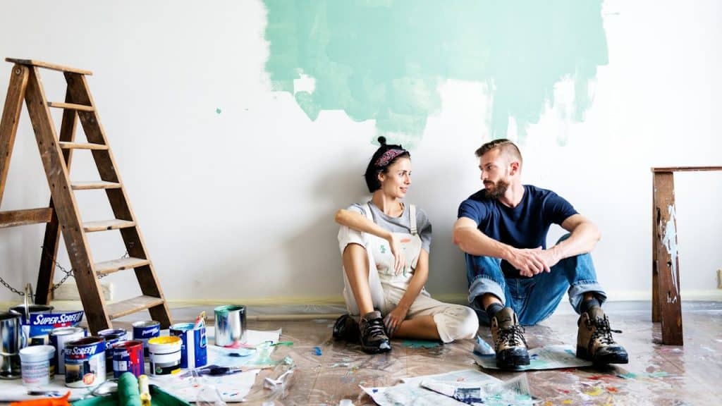 A couple looking at each other as they sit on the floor to take a break from repainting their living room.