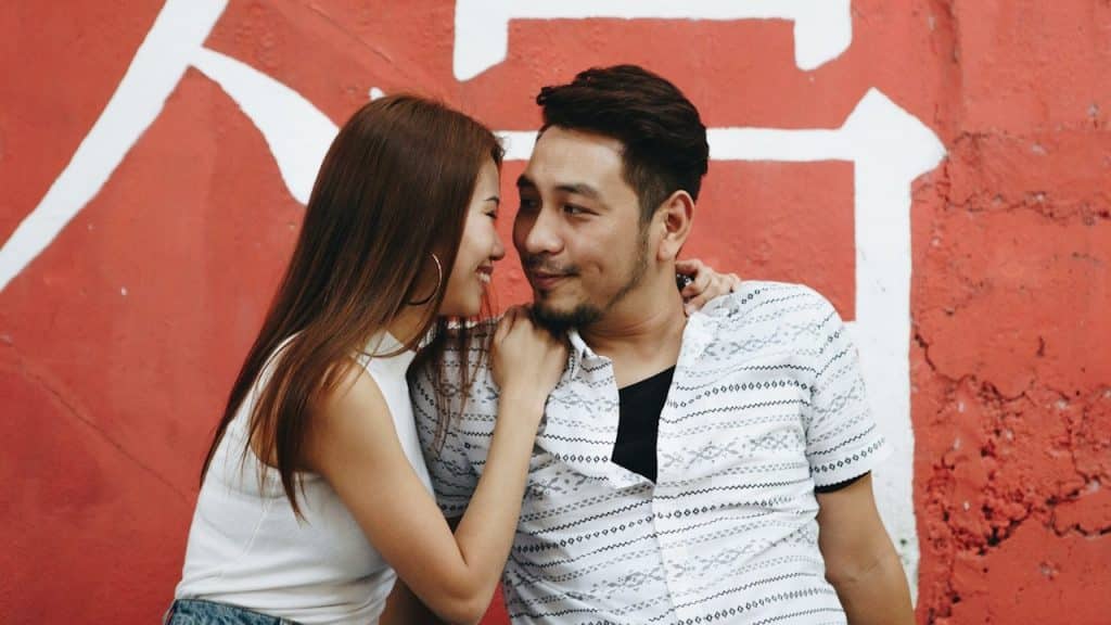 A woman smiling and whispering something in a smiling man’s ear.