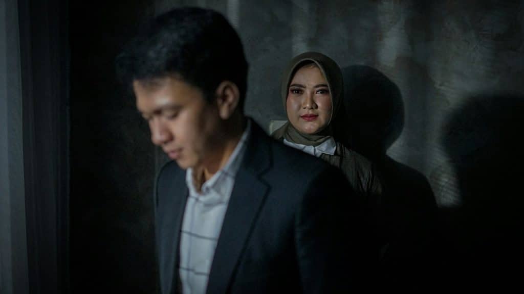 A man stares down while a woman looks at the camera in the background and smiles.